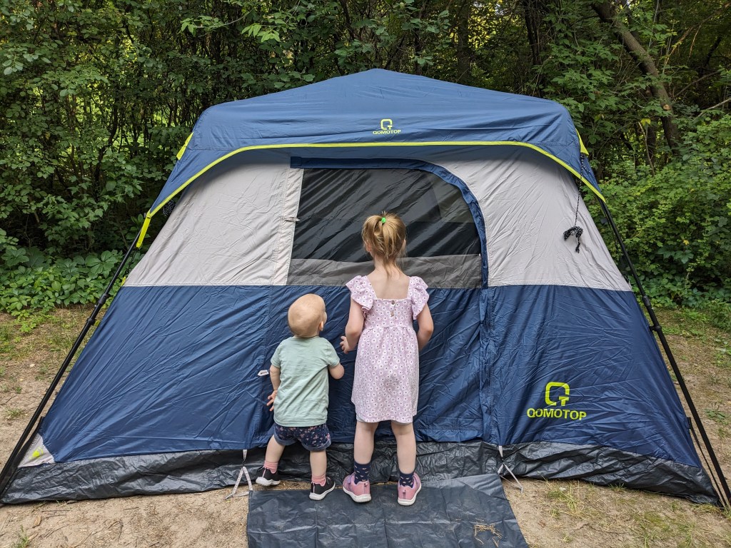 Two kids standing in front of a tent outdoors