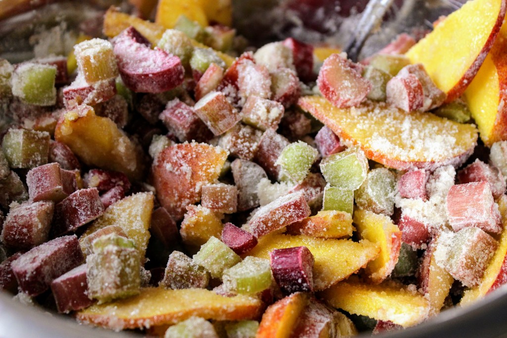 Cut rhubarb and peaches covered in sugar and flour in preparation for baking a rhubarb peach crisp.