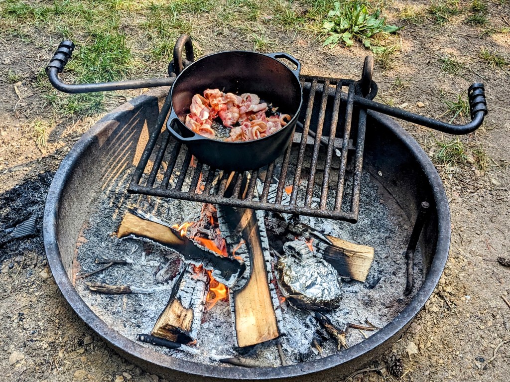 Bacon cooking in a Dutch oven over the fire.